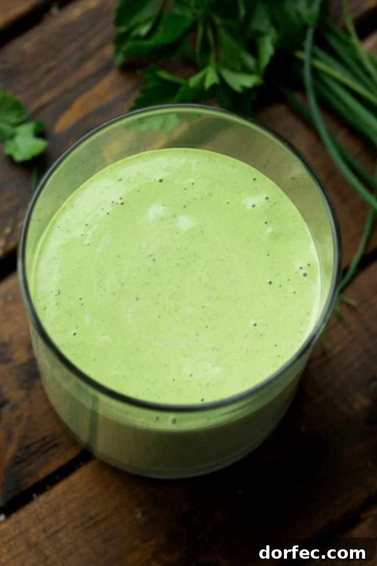 A top-down photo of a clear glass container filled with rich, green creamy basil salad dressing, inviting and fresh.