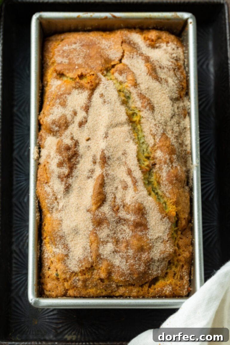 A beautiful photo of a whole loaf of golden brown banana zucchini bread, still in its pan and lightly dusted with cinnamon sugar, showcasing its perfect bake.