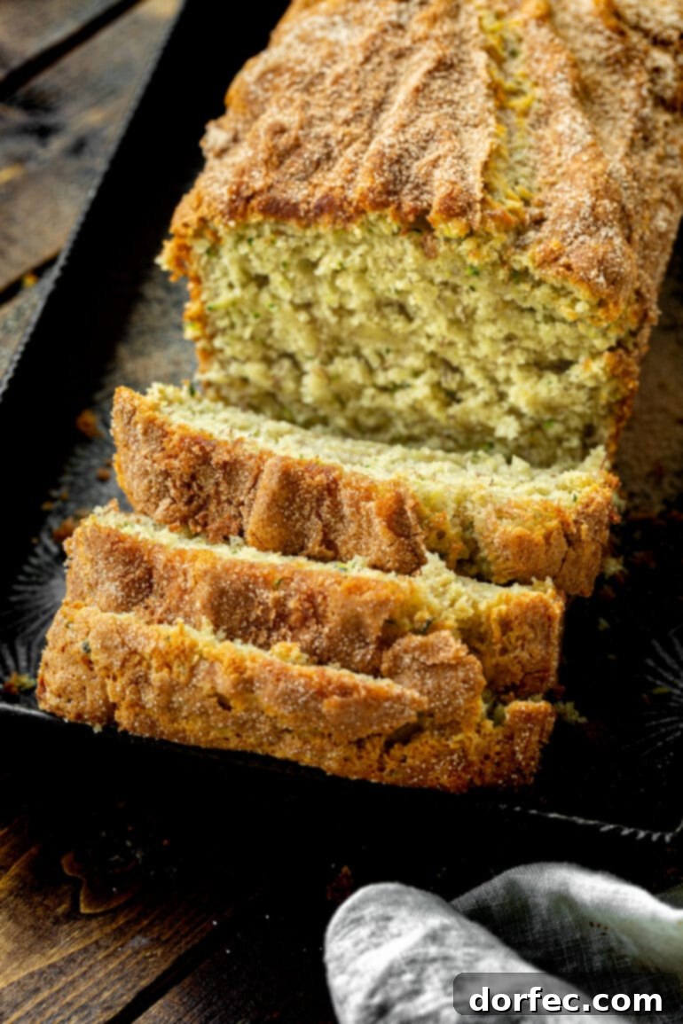A close-up photo of a baked loaf of golden banana zucchini bread, with the first few slices carefully cut and tipped over, revealing its soft, moist interior.