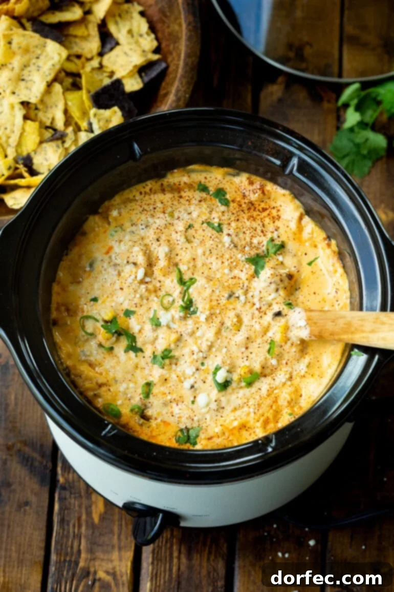 A small crockpot filled with creamy Mexican street corn dip, adorned with a wooden spoon and ready for guests to enjoy.