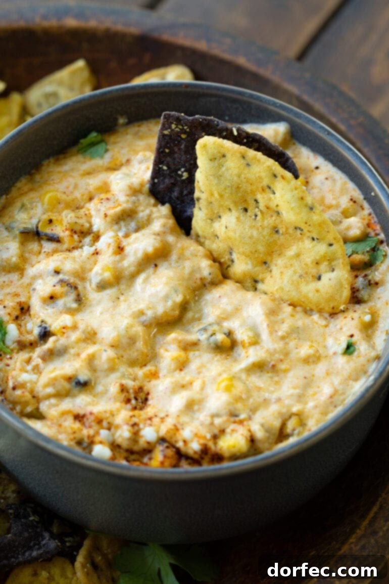 Two crunchy tortilla chips dipped deeply into a vibrant bowl of creamy Mexican street corn dip, ready for a delectable bite.