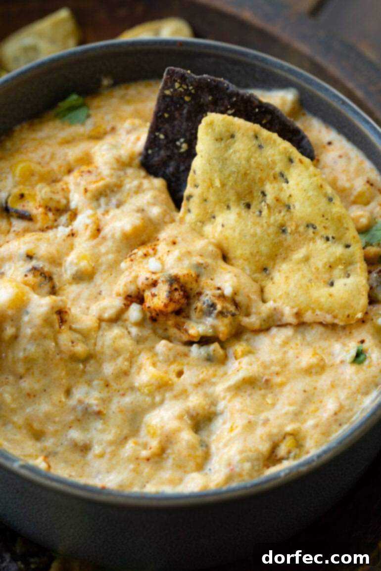 A bowl of creamy Mexican street corn dip with two tortilla chips perfectly submerged, inviting a delicious tasting experience.