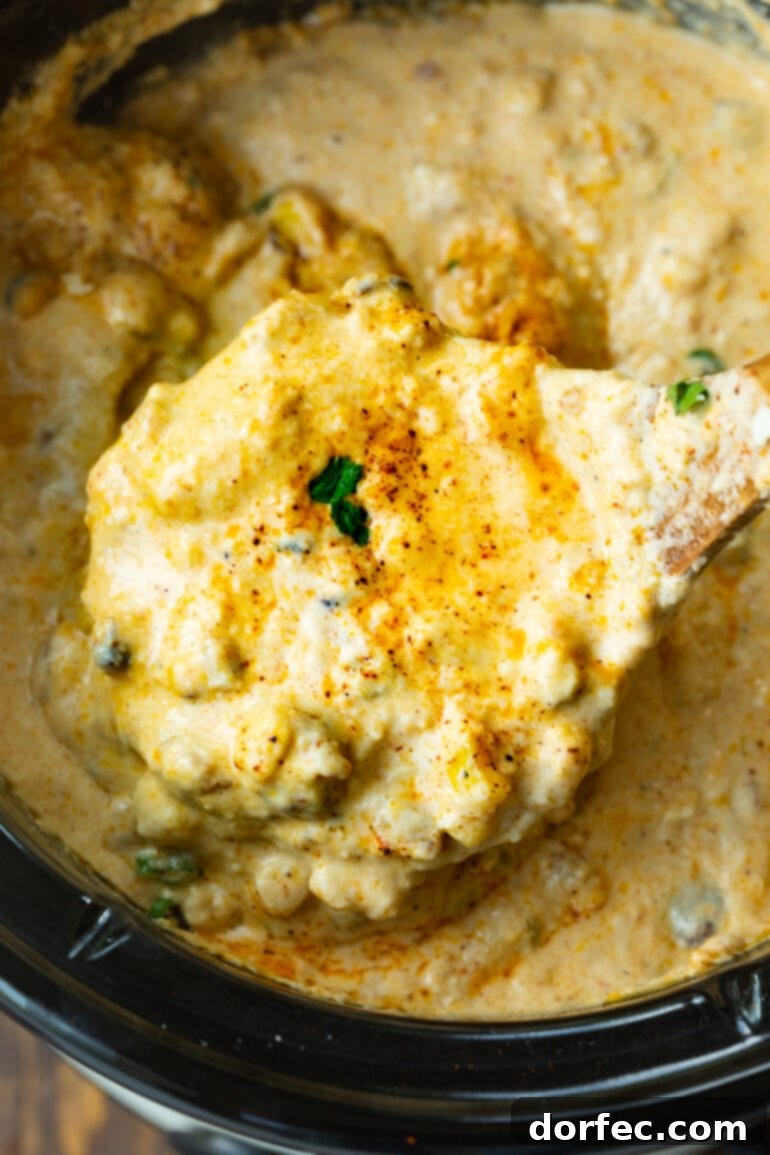 A wooden spoon lifting a generous spoonful of creamy Mexican street corn dip out of a crock pot, showcasing its delectable, melted texture.