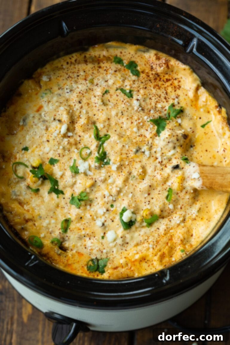A wooden spoon actively stirring a crock pot full of Mexican street corn dip, showing the delicious, ongoing preparation process.