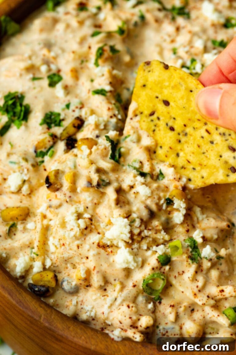 Zesty Mexican Street Corn Dip 3 a close up photo of someone dipping a tortilla chip into a bowl of Mexican corn dip.