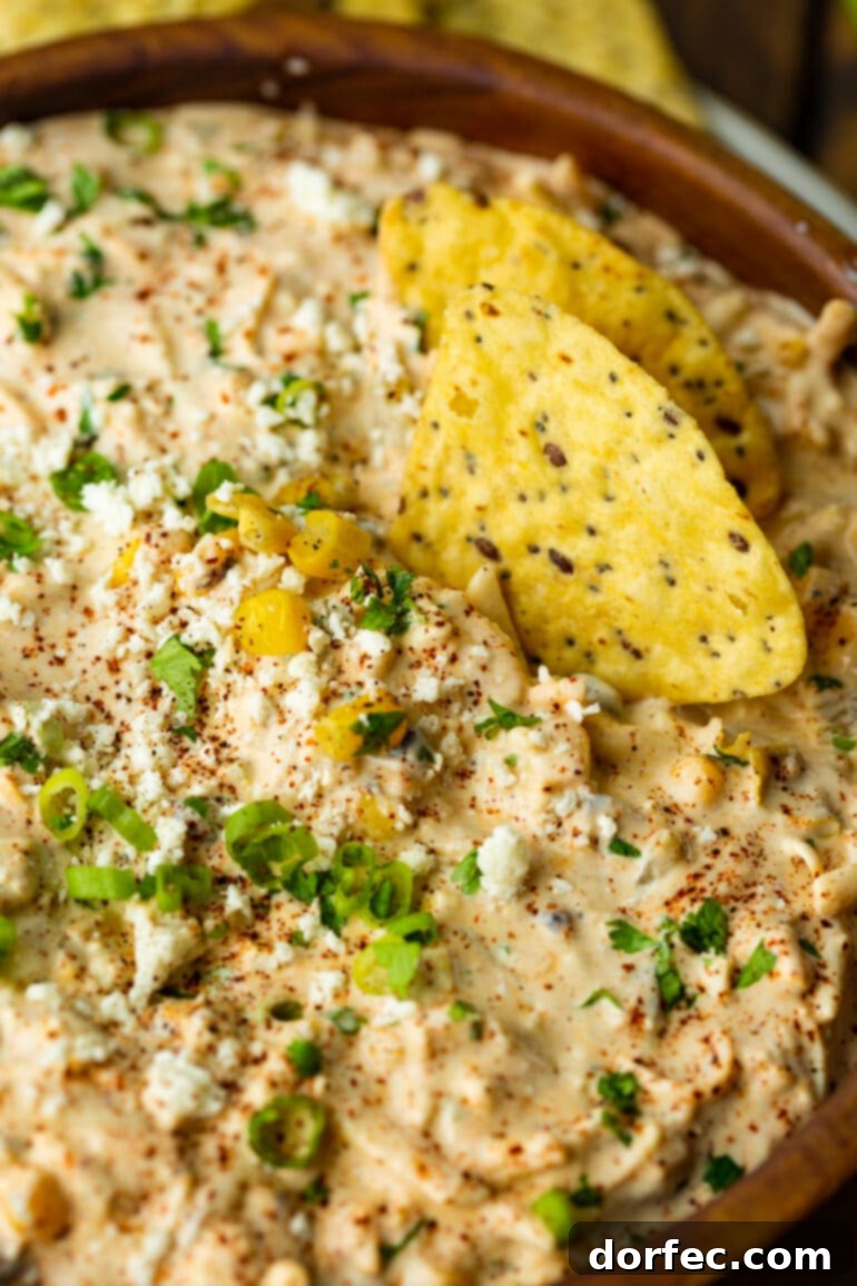 Zesty Mexican Street Corn Dip 7 a photo of a corn tortilla stuck into a bowl of mexican corn dip topped with diced green onions and pieces of corn.