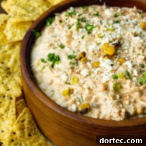 a photo of a large wooden bowl full of Mexican corn dip with tortilla chips scattered around the bowl.