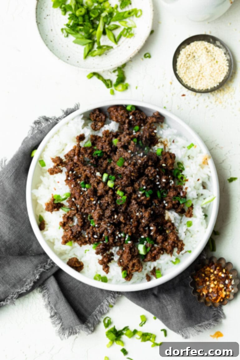 A photo taken over the top of a large bowl of steamed white rice topped with Korean ground beef, garnished with fresh scallions.