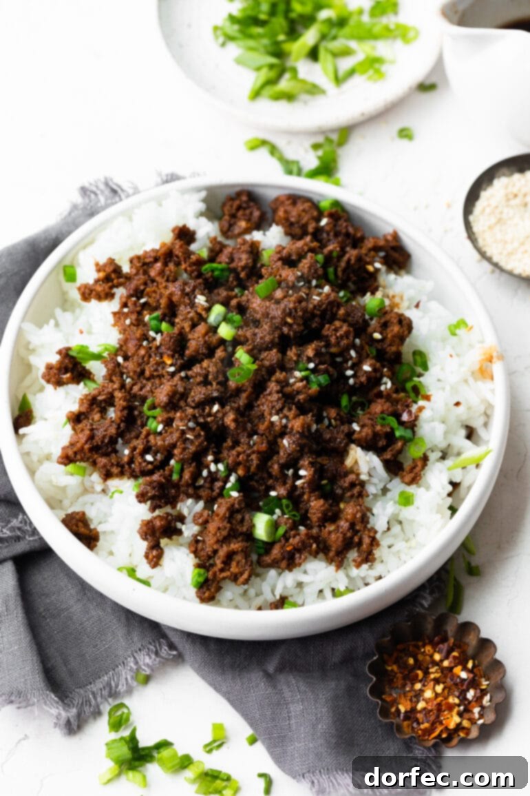 A photo of a large bowl of cooked white rice topped with saucy Korean ground beef, sliced scallions and sesame seeds, showcasing a beautifully prepared meal.