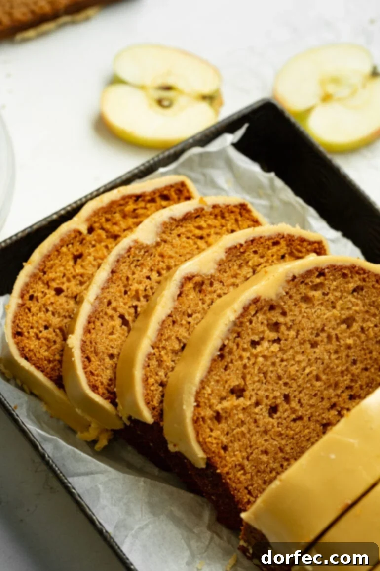 Several slices of moist apple bread, generously drizzled with warm brown sugar icing, stacked invitingly on a rustic wooden board. The golden-brown crust and tender interior highlight the comforting nature of this fall dessert.
