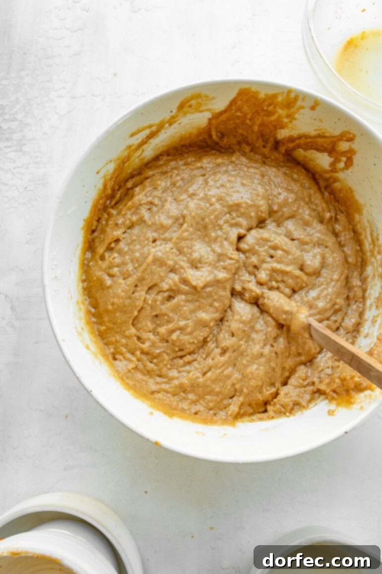 A large mixing bowl filled with rich, spiced apple bread batter, with a wooden spoon resting inside, ready for the oven.