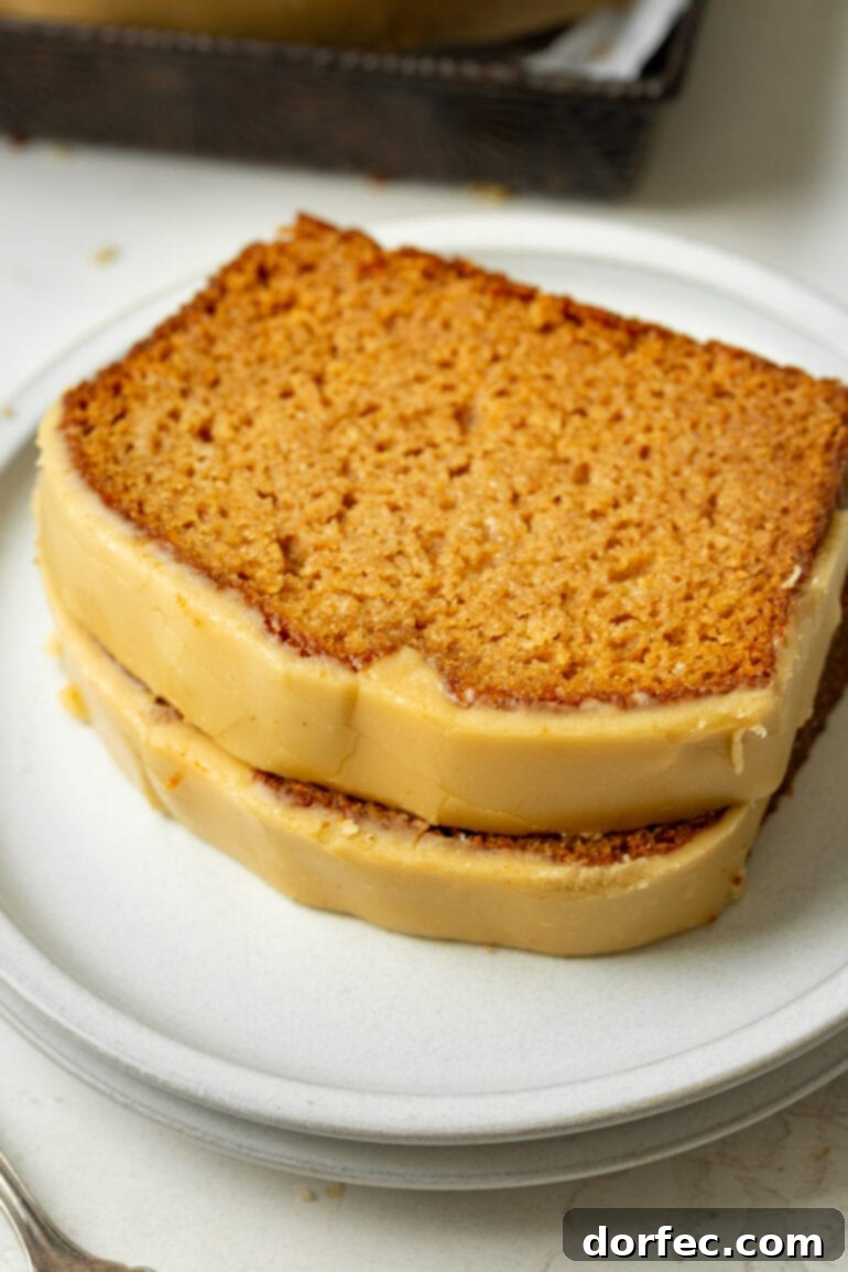 Two generous slices of homemade apple bread, beautifully stacked and lavishly topped with glistening brown sugar icing, presented on a pristine white plate.