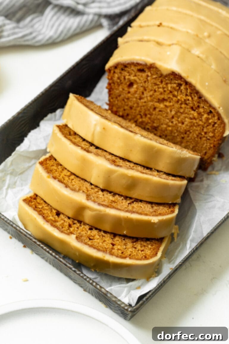 A beautifully baked loaf of apple bread, generously adorned with a rich brown sugar icing, with four inviting slices carefully removed and leaning against the main loaf.