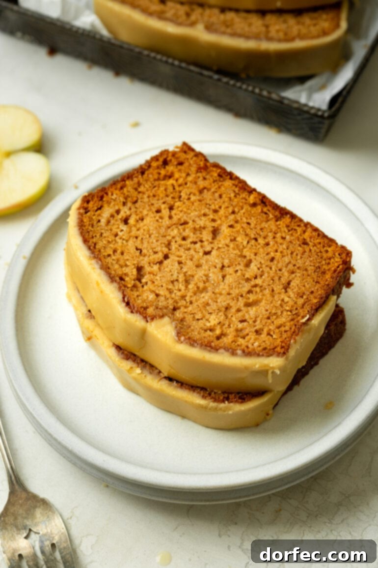Two enticing slices of homemade apple bread, generously covered in a glossy brown sugar icing, stacked on top of each other on a delicate white dessert plate.