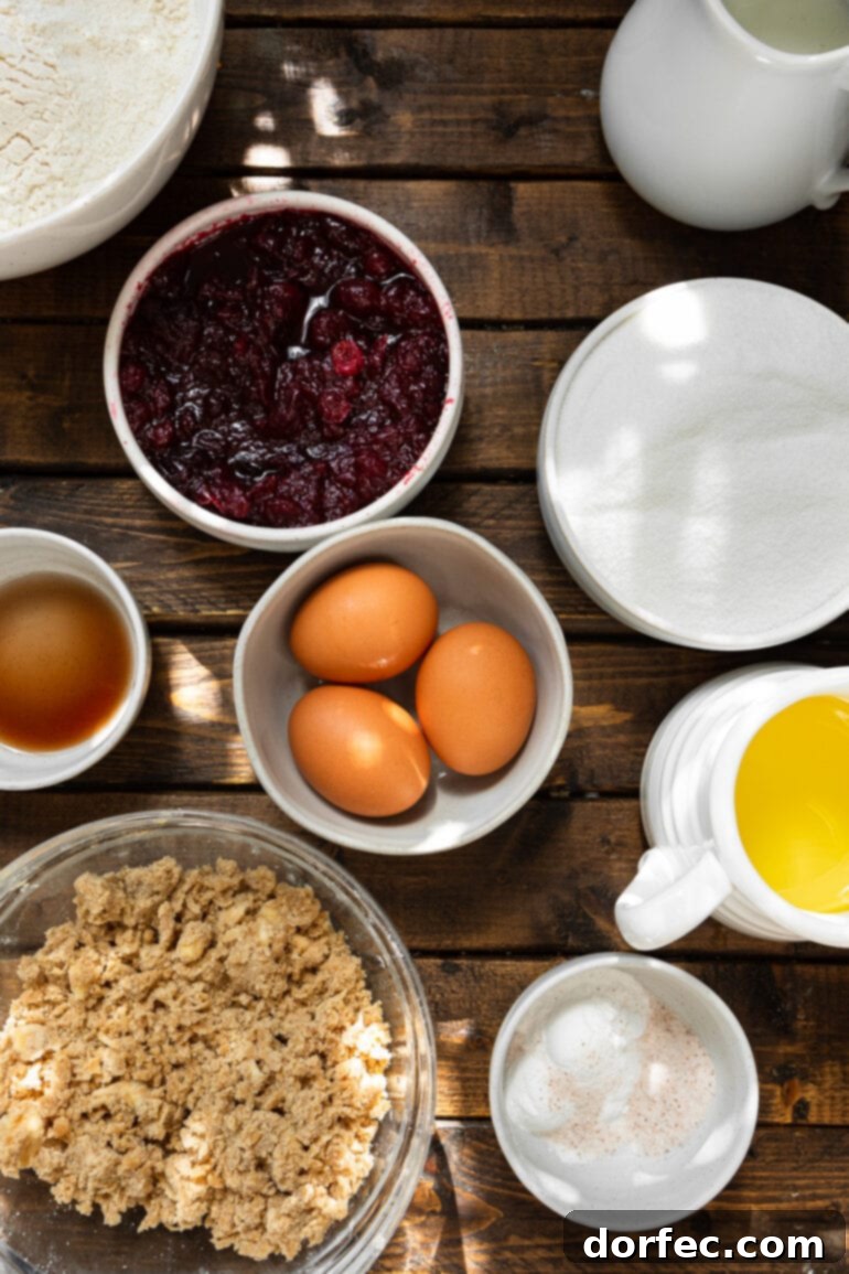 An overhead shot showcasing all the essential ingredients for cranberry sauce muffins, neatly arranged in separate bowls, including butter, eggs, sugar, flour, vanilla, and cranberry sauce.