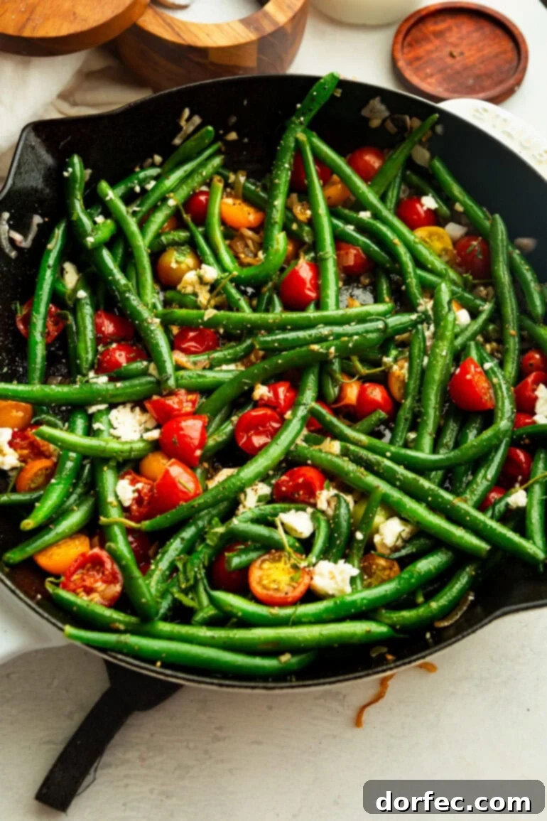 A vibrant pan brimming with sautéed green beans and a colorful assortment of cherry tomatoes, finished with fresh herbs and a sprinkle of cheese.