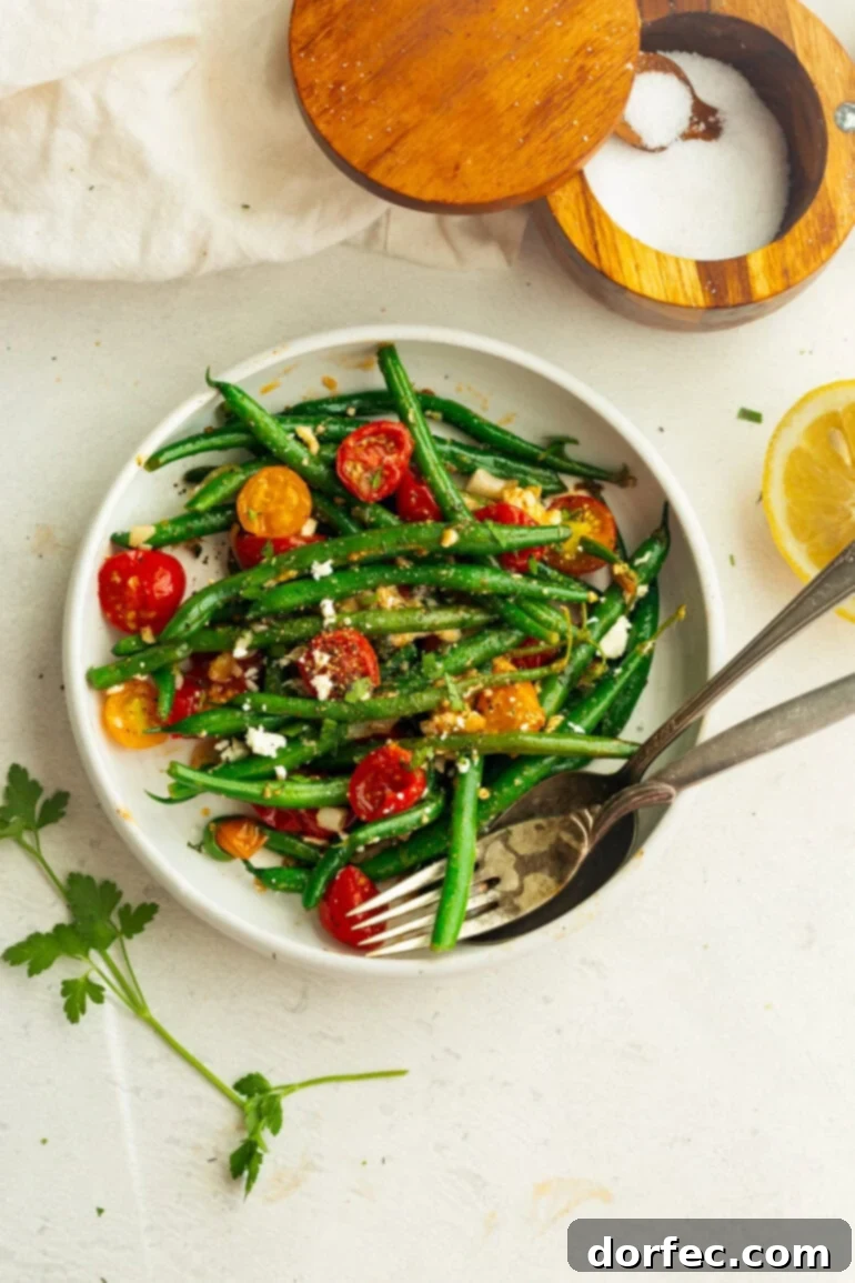 A white bowl showcasing sautéed green beans and halved cherry tomatoes, elegantly garnished with crumbled feta cheese and fresh herbs, with a fork gently resting.
