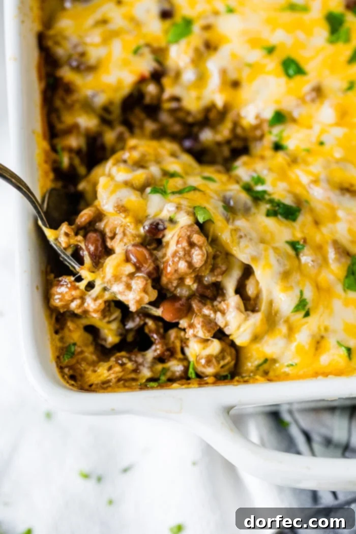 Your Weekly Meal Plan: September 18-24 3 A white ceramic casserole dish brimming with a Mexican cheesy ground beef and rice casserole, with a large serving spoon scooping out a portion, revealing the savory layers of seasoned beef, fluffy rice, and rich, melted cheese beneath a golden-brown crust.