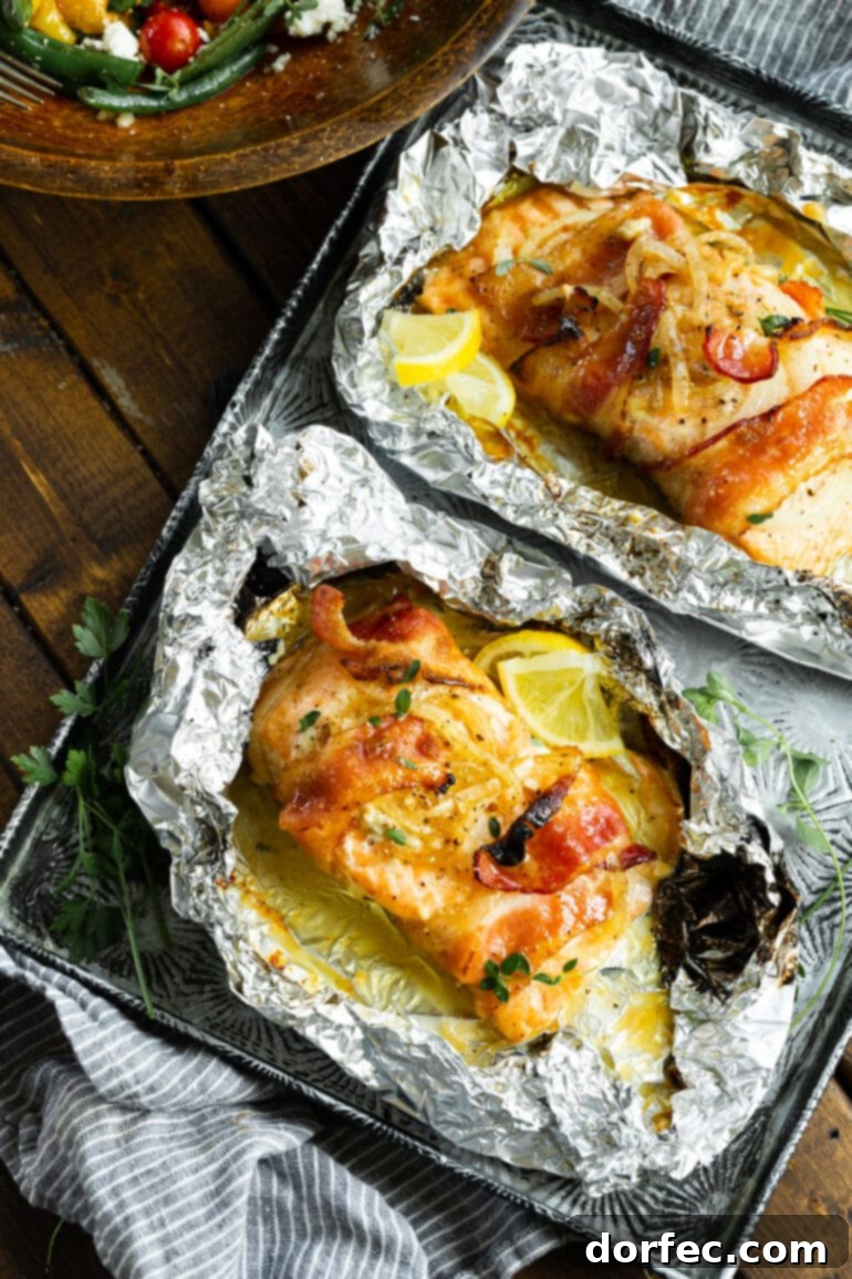 Two succulent baked salmon fillets, each meticulously wrapped in crispy bacon and topped with caramelized onions and bright lemon wedges, peeking from their foil packets.