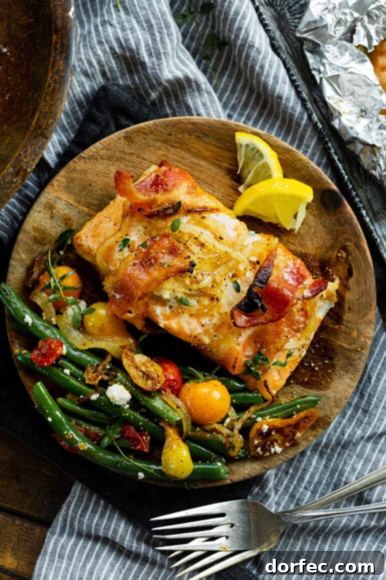 An overhead view of a beautifully baked mustard maple salmon fillet, wrapped in bacon, served on a wooden plate with a vibrant side of sautéed green beans and cherry tomatoes.