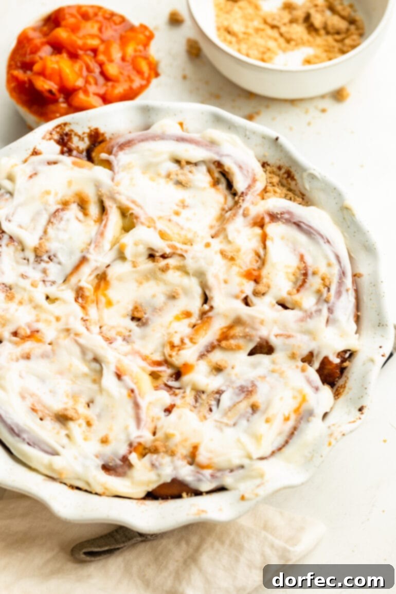 Peach Cobbler Swirl Buns 11 A circular baking dish filled with baked peach cobbler cinnamon rolls, generously topped with a rich cream cheese frosting, ready to be served.