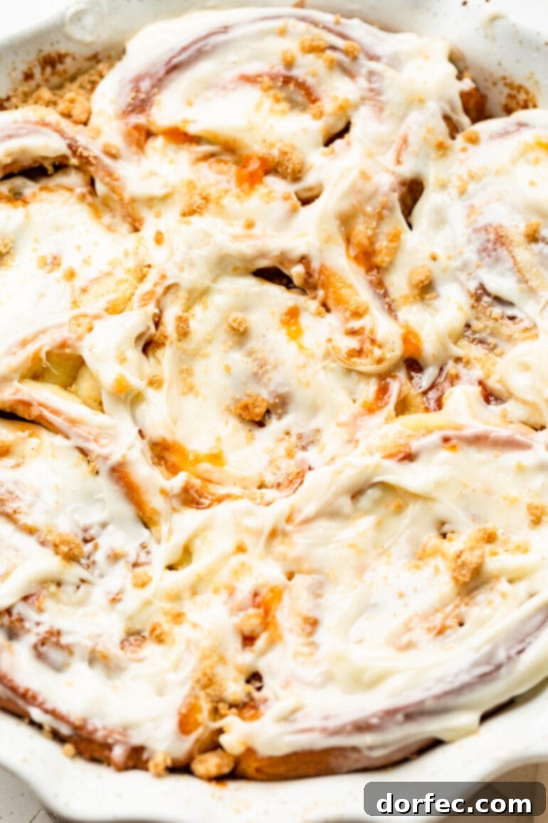 Peach Cobbler Swirl Buns 12 A baking dish filled with beautifully baked peach cinnamon rolls, lovingly topped with a generous layer of peach cream cheese frosting, promising a delectable experience.