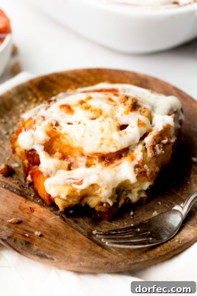 Peach Cobbler Swirl Buns 13 A beautifully baked single cinnamon roll resting on a small wooden dessert plate, highlighting its perfect swirls and inviting texture.