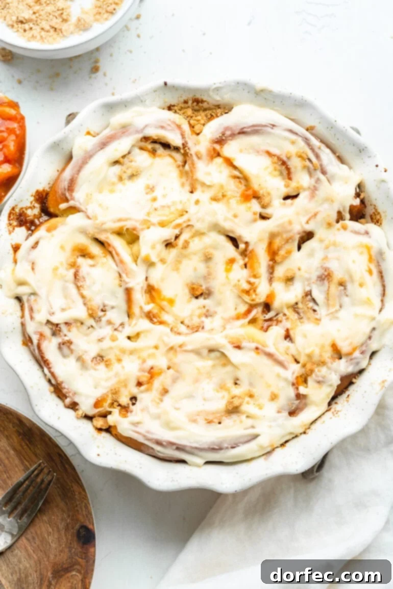 Peach Cobbler Swirl Buns 3 A circular baking dish filled with golden-brown, frosted peach cobbler cinnamon rolls, inviting you to take a bite.