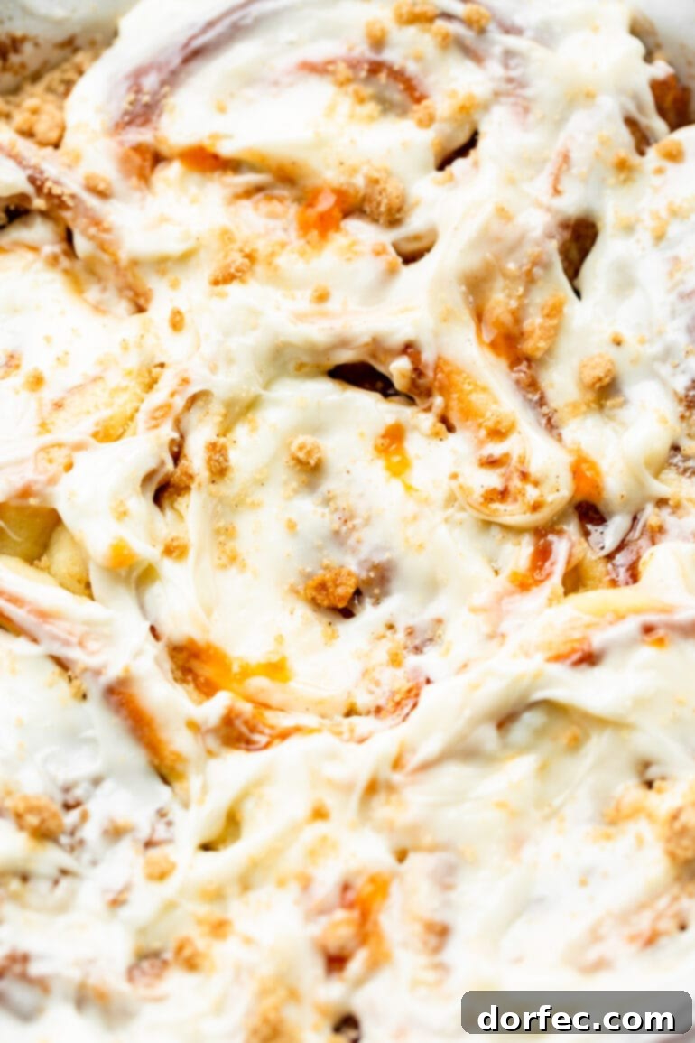 Peach Cobbler Swirl Buns 4 A pan overflowing with freshly baked peach cinnamon rolls, glistening under a thick layer of creamy peach cream cheese frosting, ready to be enjoyed.