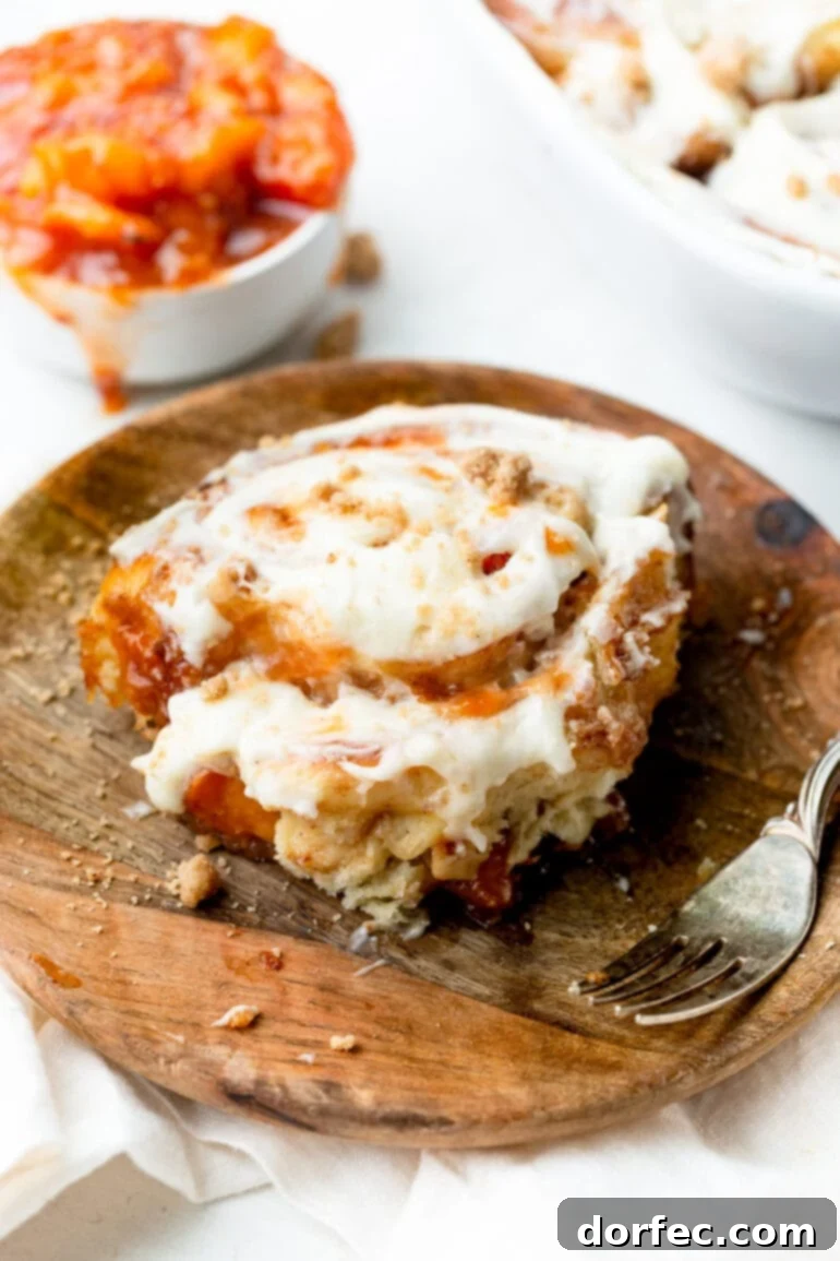 Peach Cobbler Swirl Buns 5 A single, perfectly baked peach cobbler cinnamon roll on a small wooden plate, a fork resting beside it, beckoning for a taste.