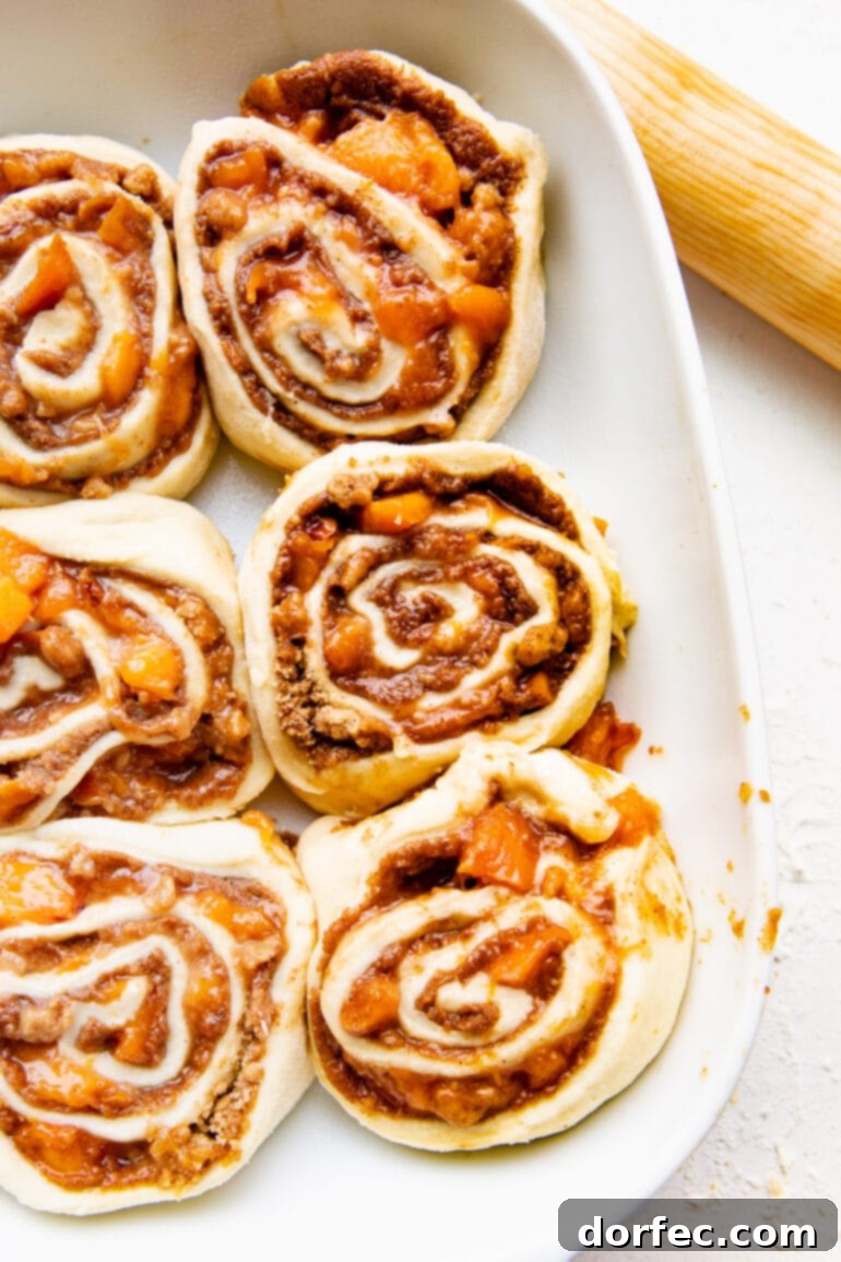 Peach Cobbler Swirl Buns 9 A baking dish filled with unbaked peach cobbler cinnamon rolls, snugly arranged and ready for their second rise before baking.