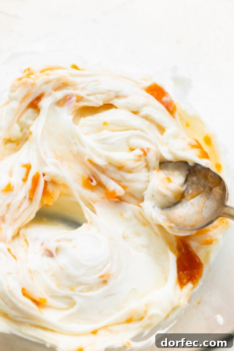 Peach Cobbler Swirl Buns 10 A close-up of a golden-baked cinnamon roll being generously topped with creamy white cream cheese frosting, showing its appealing texture.