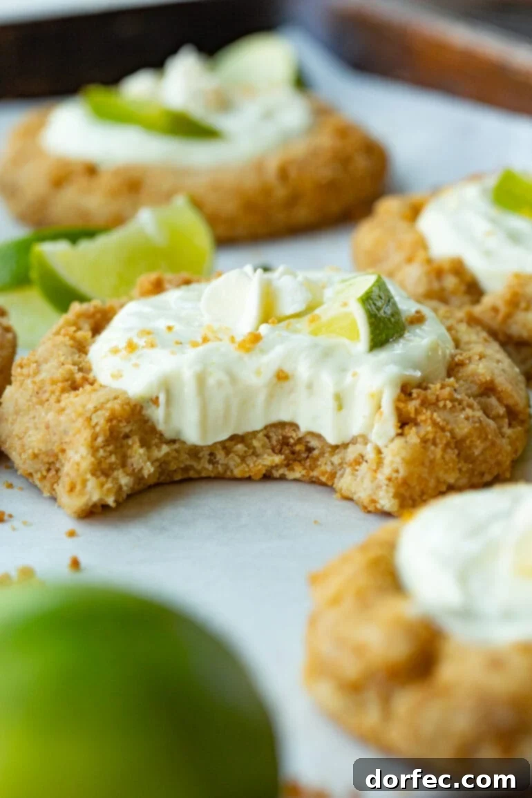 Key Lime Pie Crumbl Cookies 2 A photo of a key lime pie cookie with a bite taken out of it, revealing the creamy filling inside the graham cracker crust cookie. It's topped with a small slice of fresh lime.