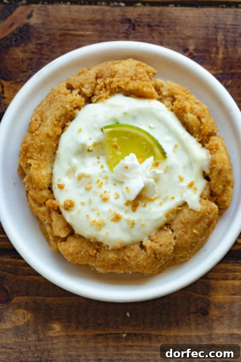 Key Lime Pie Crumbl Cookies 3 A photo taken from above, showcasing a key lime pie cookie topped with a wedge of fresh lime and a small dollop of whipped cream.