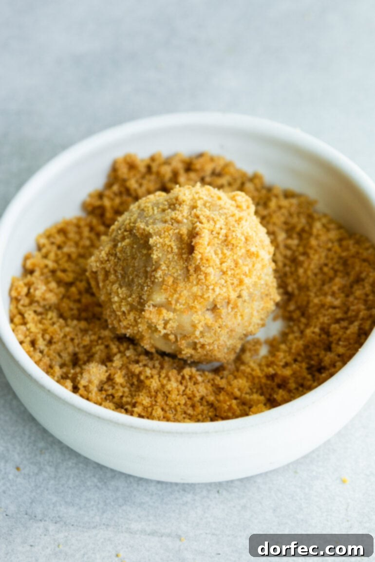 Key Lime Pie Crumbl Cookies 5 A photo of a cookie dough ball being rolled in a shallow dish full of graham cracker crumbs, showing the homemade crust being applied.
