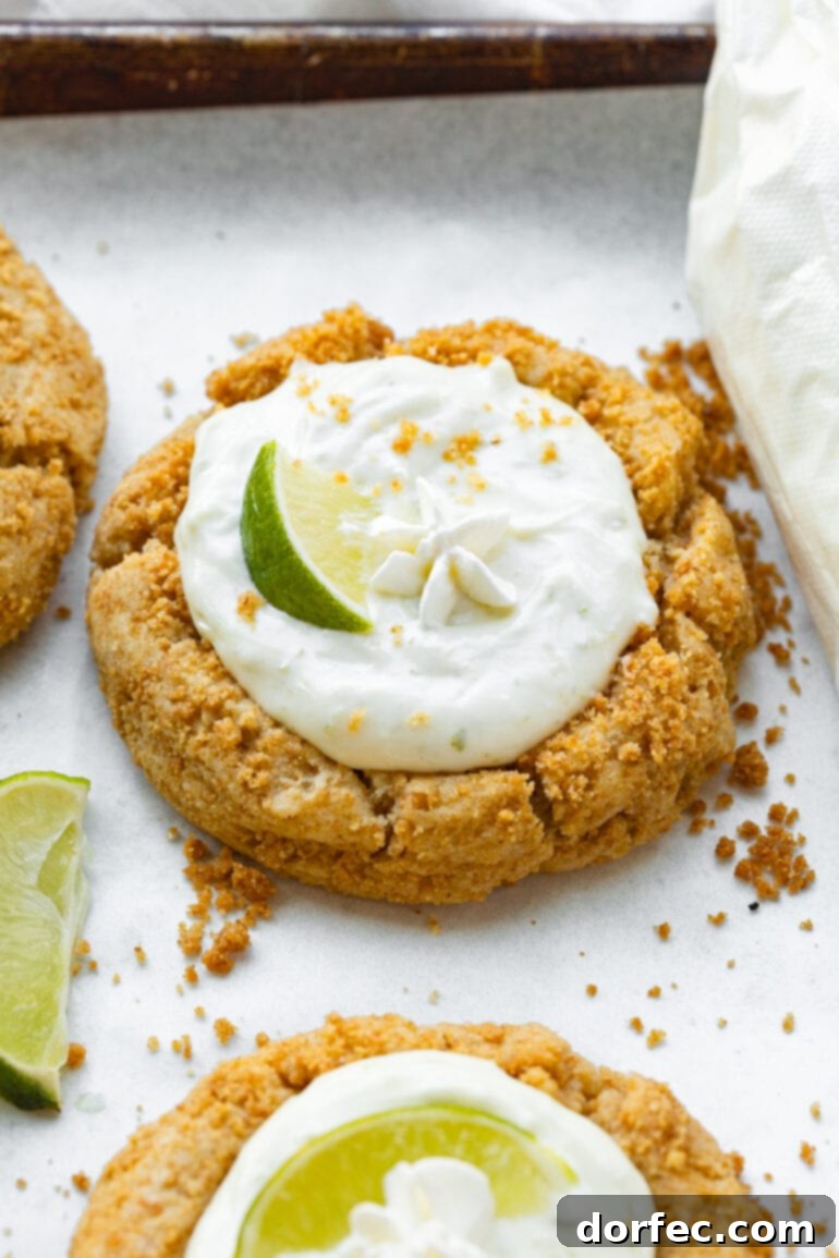 Key Lime Pie Crumbl Cookies 6 A photo of a baked graham cracker crust cookie filled with creamy key lime pie filling, topped with a small lime wedge and whipped cream.