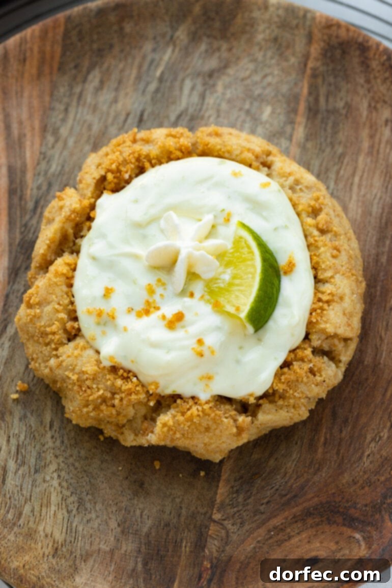 Key Lime Pie Crumbl Cookies 7 A photo of a baked graham cracker crust cookie filled with creamy key lime pie filling, topped with a small lime wedge and sprinkled with graham cracker crumbs.