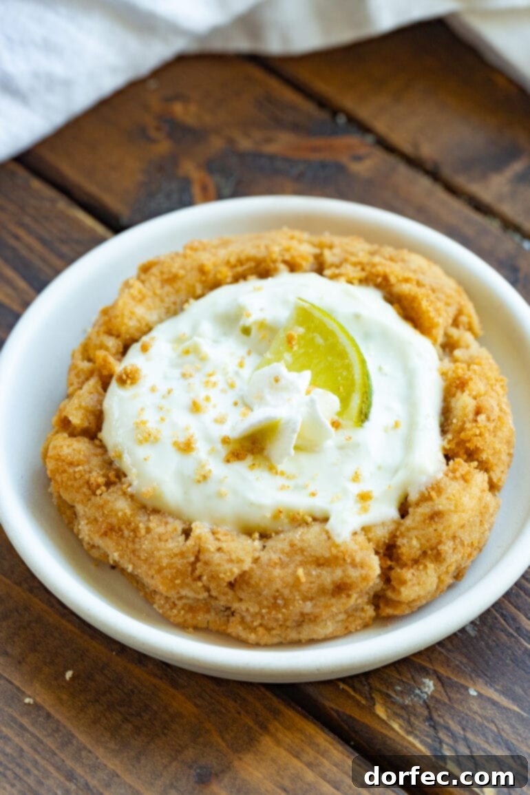 Key Lime Pie Crumbl Cookies 8 A photo of a golden baked graham cracker cookie filled with key lime pie filling and topped with a small lime wedge and a dollop of whipped cream, inviting indulgence.