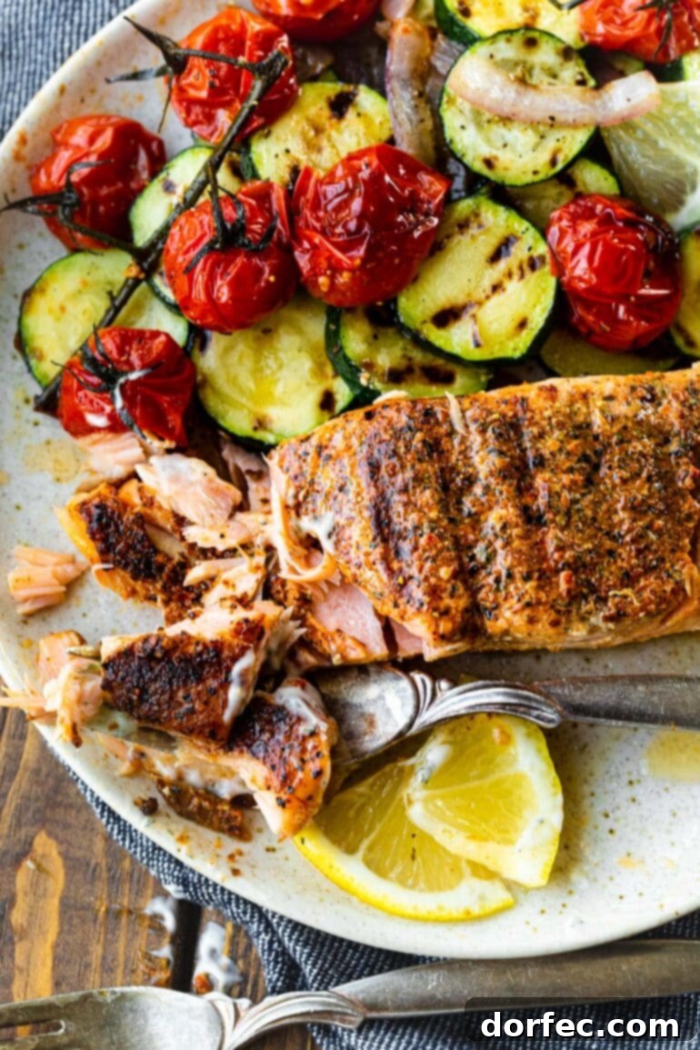 A perfectly grilled salmon fillet, flaky and tender, served alongside a vibrant medley of grilled vegetables and fresh lemon slices. The salmon exhibits a beautiful char, hinting at its smoky flavor.