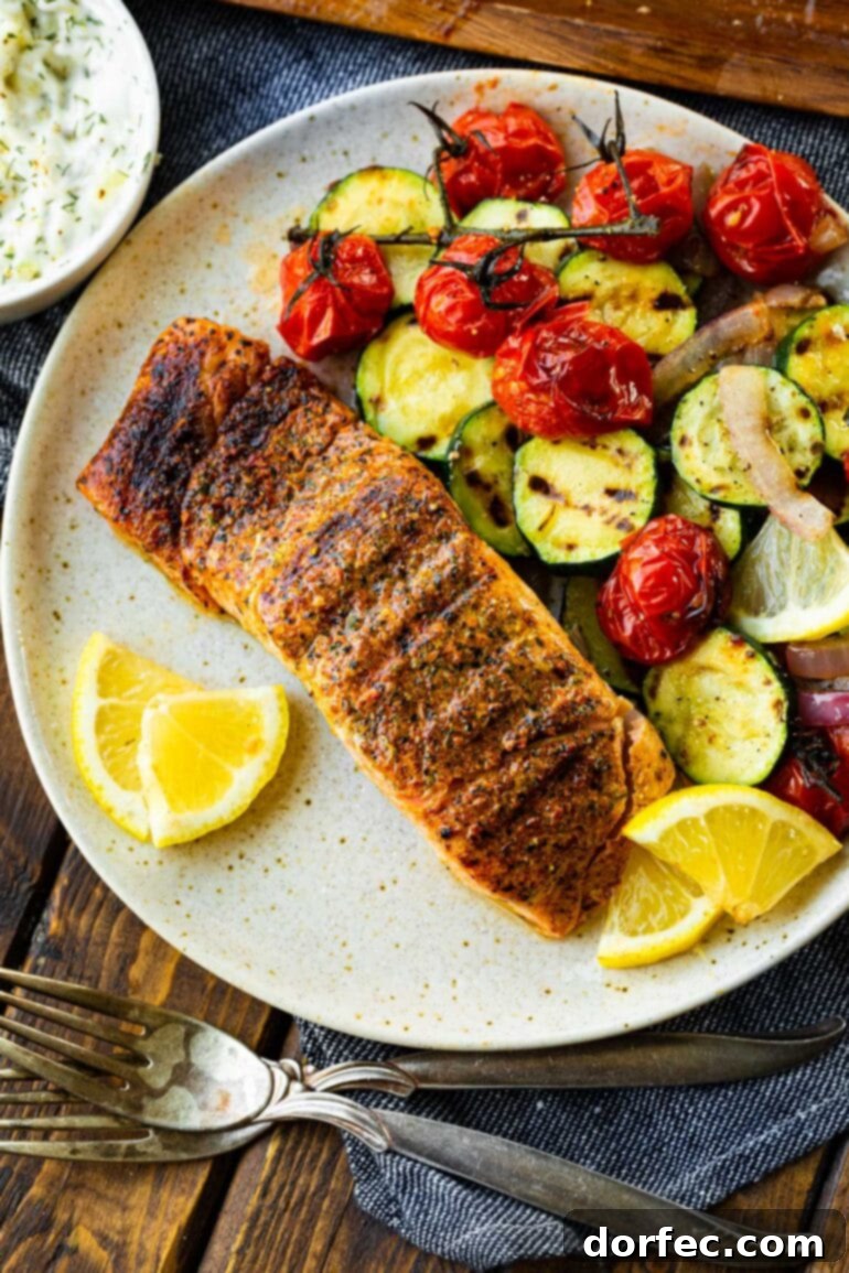 A seasoned grilled salmon fillet rests on a dinner plate, accompanied by a side of colorful grilled vegetables and wedges of fresh lemon, ready to be enjoyed.
