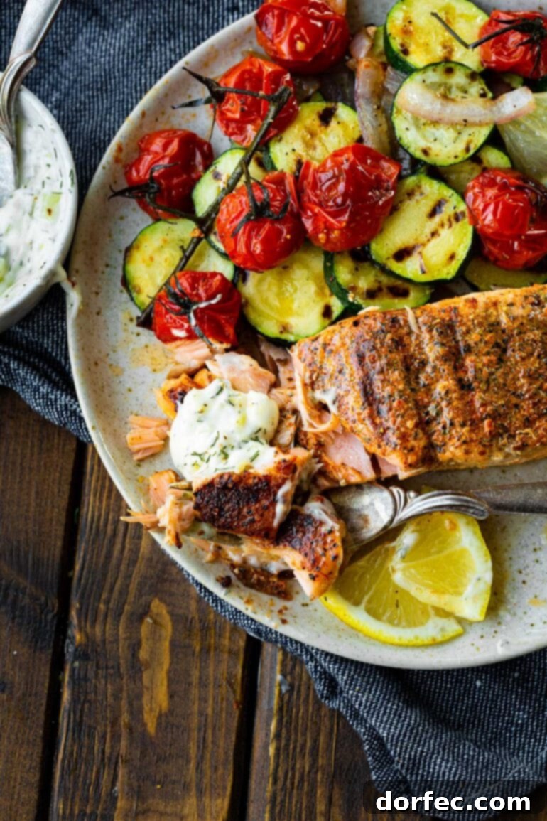 A succulent grilled salmon fillet, expertly flaked open with a fork, is served with a vibrant array of grilled vegetables, highlighting its tender, moist texture.
