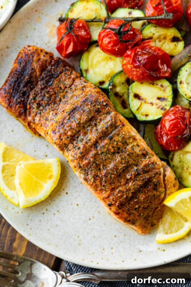 A perfectly grilled salmon fillet, golden brown with crisp edges, is elegantly presented alongside vibrant lemon slices and a colorful medley of grilled zucchini and cherry tomatoes.