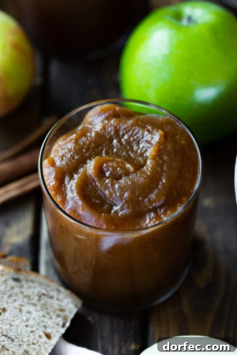 Set-It-and-Forget-It Slow Cooker Apple Butter 4 A pristine glass jar brimming with smooth, caramel-brown apple butter, with a fresh, crisp Granny Smith apple resting subtly in the background.