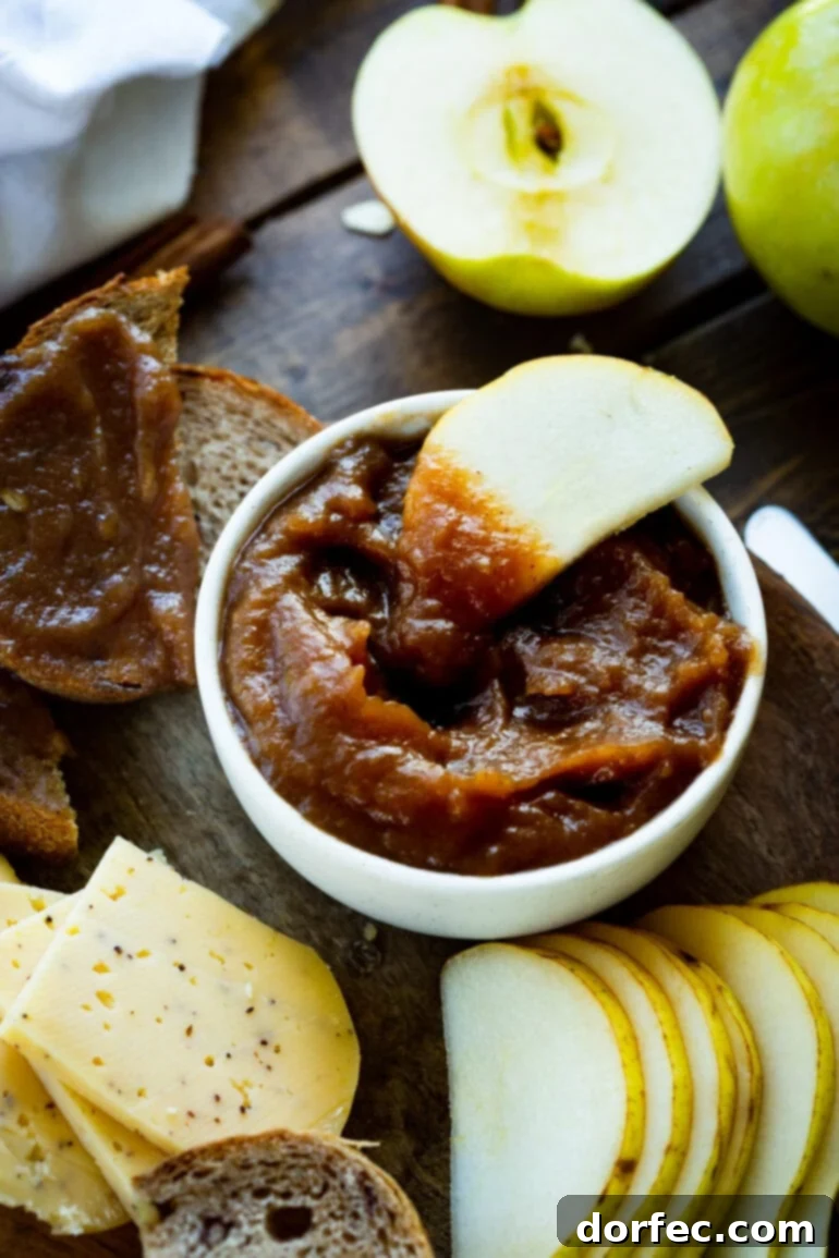 Set-It-and-Forget-It Slow Cooker Apple Butter 5 A small, inviting bowl of rich, caramel-colored apple butter, with a crisp slice of fresh apple dipped into its smooth texture, suggesting delicious pairing possibilities.