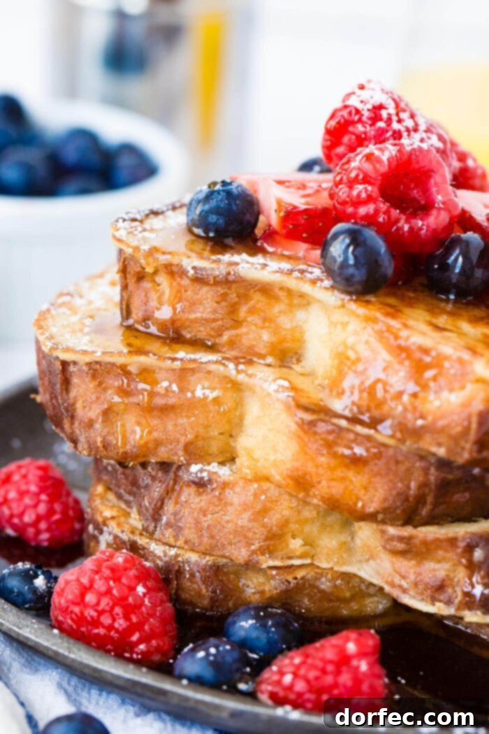 A mouth-watering photo of a stack of four golden-brown French toast slices, artfully arranged and generously drizzled with syrup, adorned with fresh, vibrant berries. A truly enticing breakfast or brunch option.