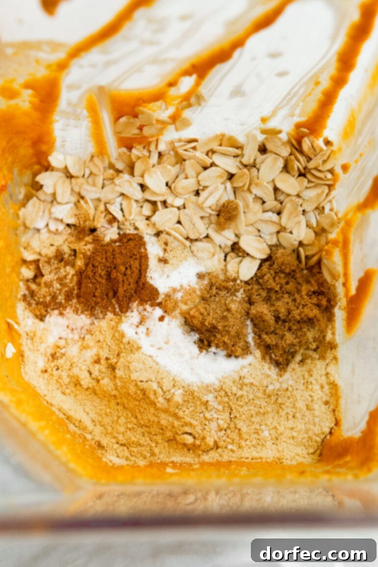 A photo of all the ingredients for a pumpkin mug cake sitting in a blender, unblended, including oats, spices, and pumpkin puree.