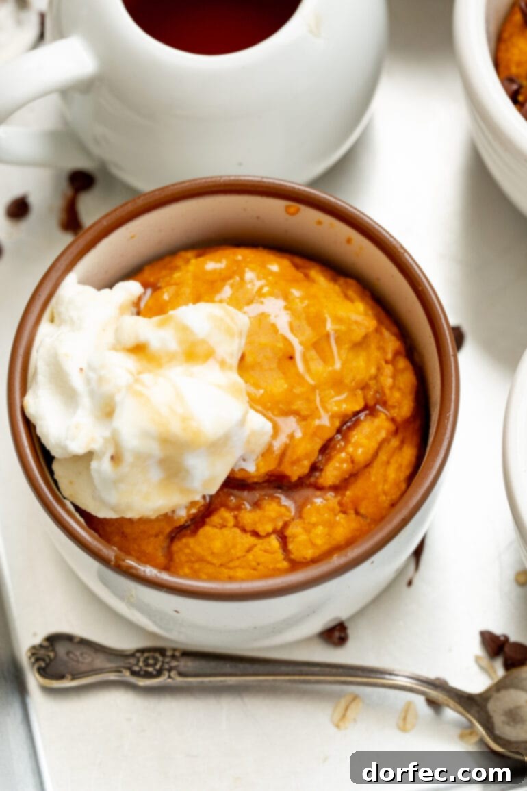 A photo of a pumpkin mug cake that has been baked and topped with a dollop of whipped cream, emphasizing its delicious and ready-to-eat state.