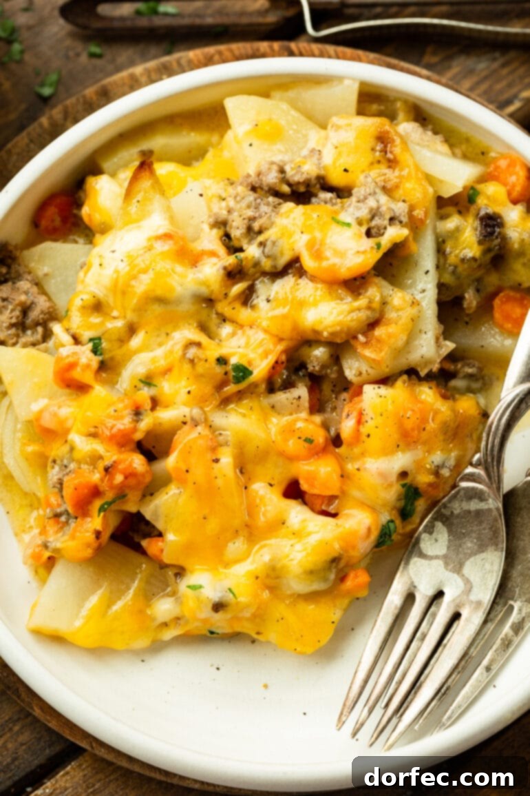 A dinner plate featuring a generous serving of creamy, cheesy ground beef and potato casserole, with two forks resting beside it, ready to be enjoyed. 