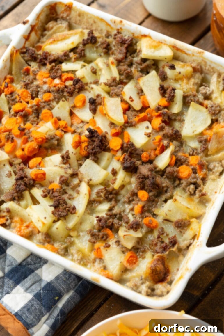 A square baking dish showcasing a medley of cooked cubed potatoes, seasoned ground beef, and vibrant sliced carrots nestled in a rich, creamy sauce. 