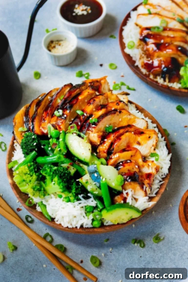 a photo of a plate of rice covered with teriyaki chicken and steamed broccoli and zucchini.